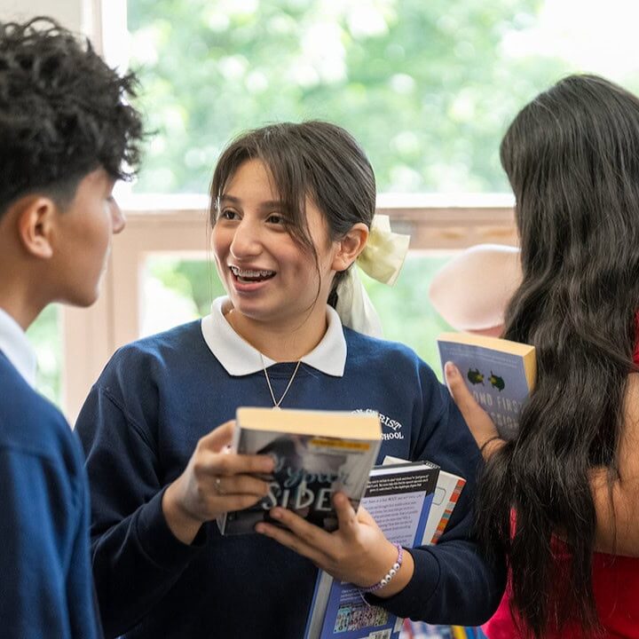 Risen Christ middle school students talking and laughing with books in hand