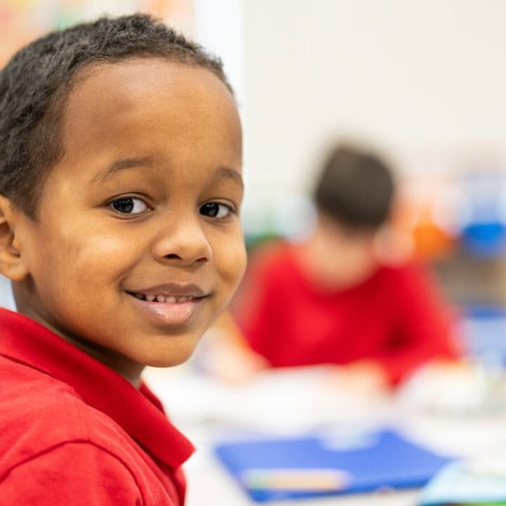 A smiling Risen Christ student in a red uniform shirt in the classroom